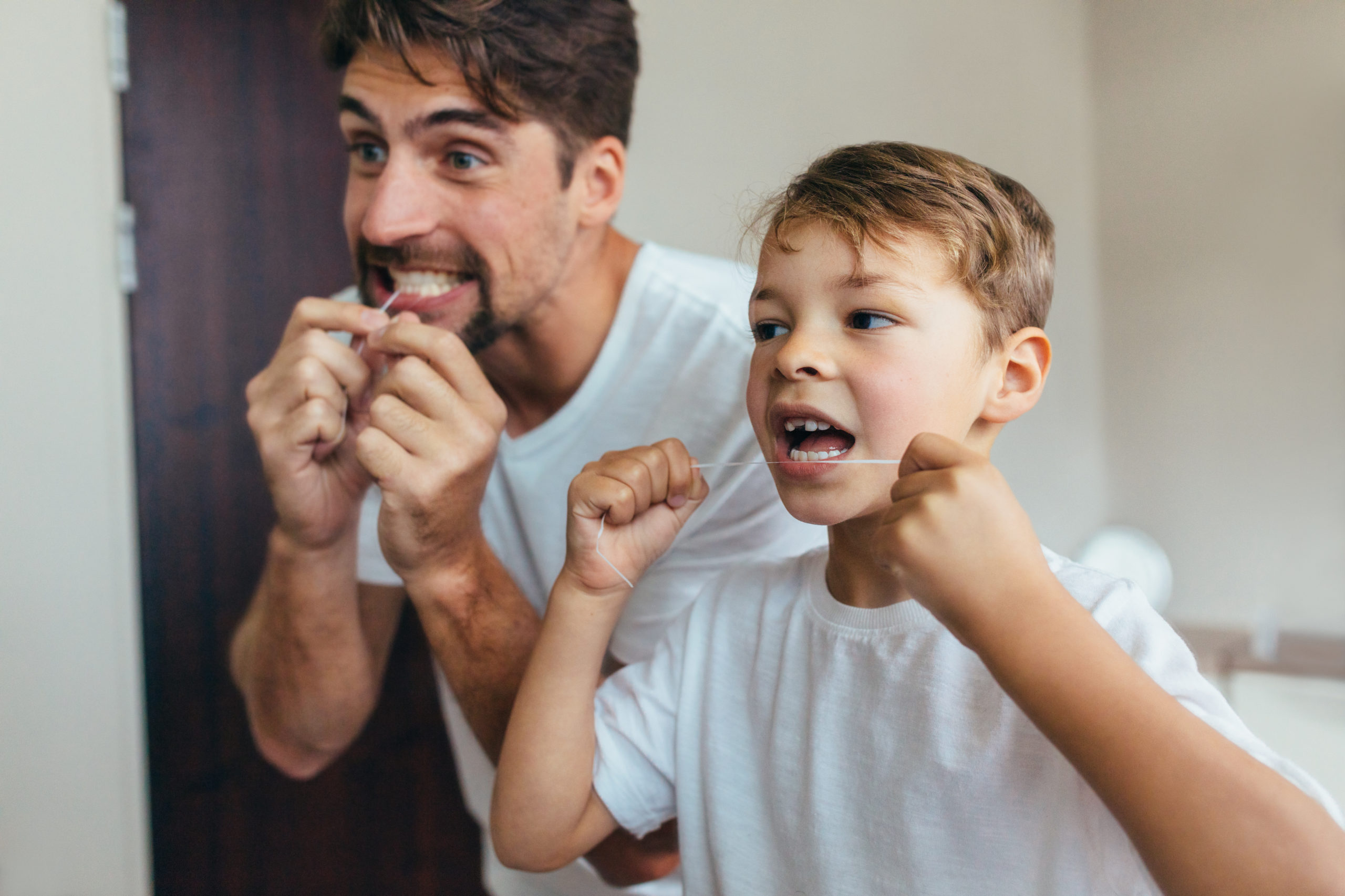 Father and son cleaning teeth with dental floss